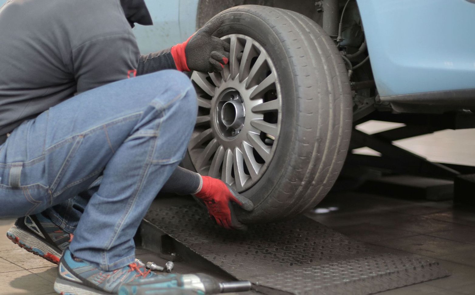 Mechanic changing a car tire indoors, using tools for vehicle maintenance.